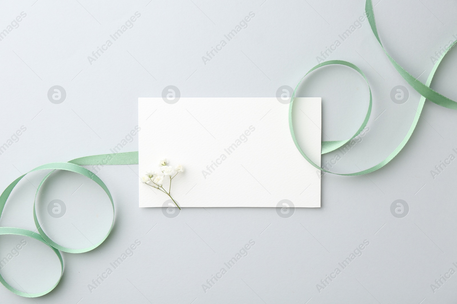 Photo of Blank card, flower and ribbon on light grey table, top view