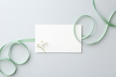 Blank card, flower and ribbon on light grey table, top view