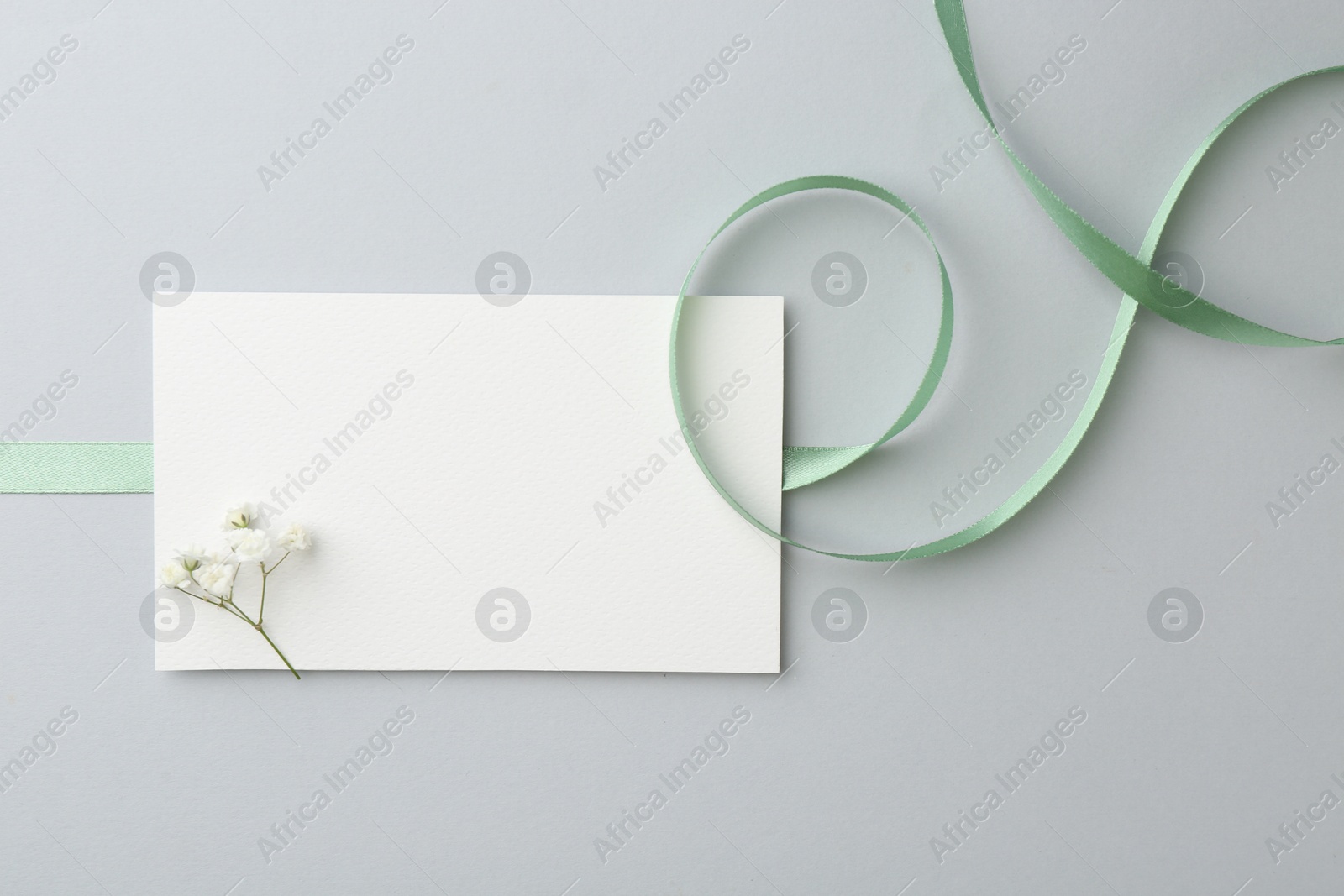 Photo of Blank card, flower and ribbon on light grey table, top view