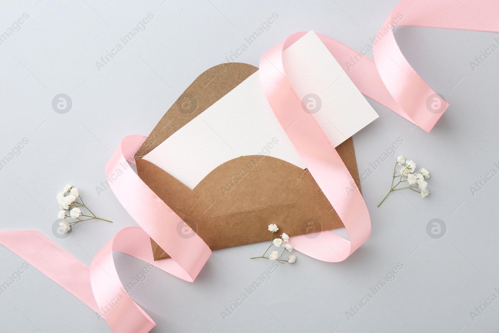 Photo of Blank card, envelope, flowers and ribbon on light grey table, flat lay