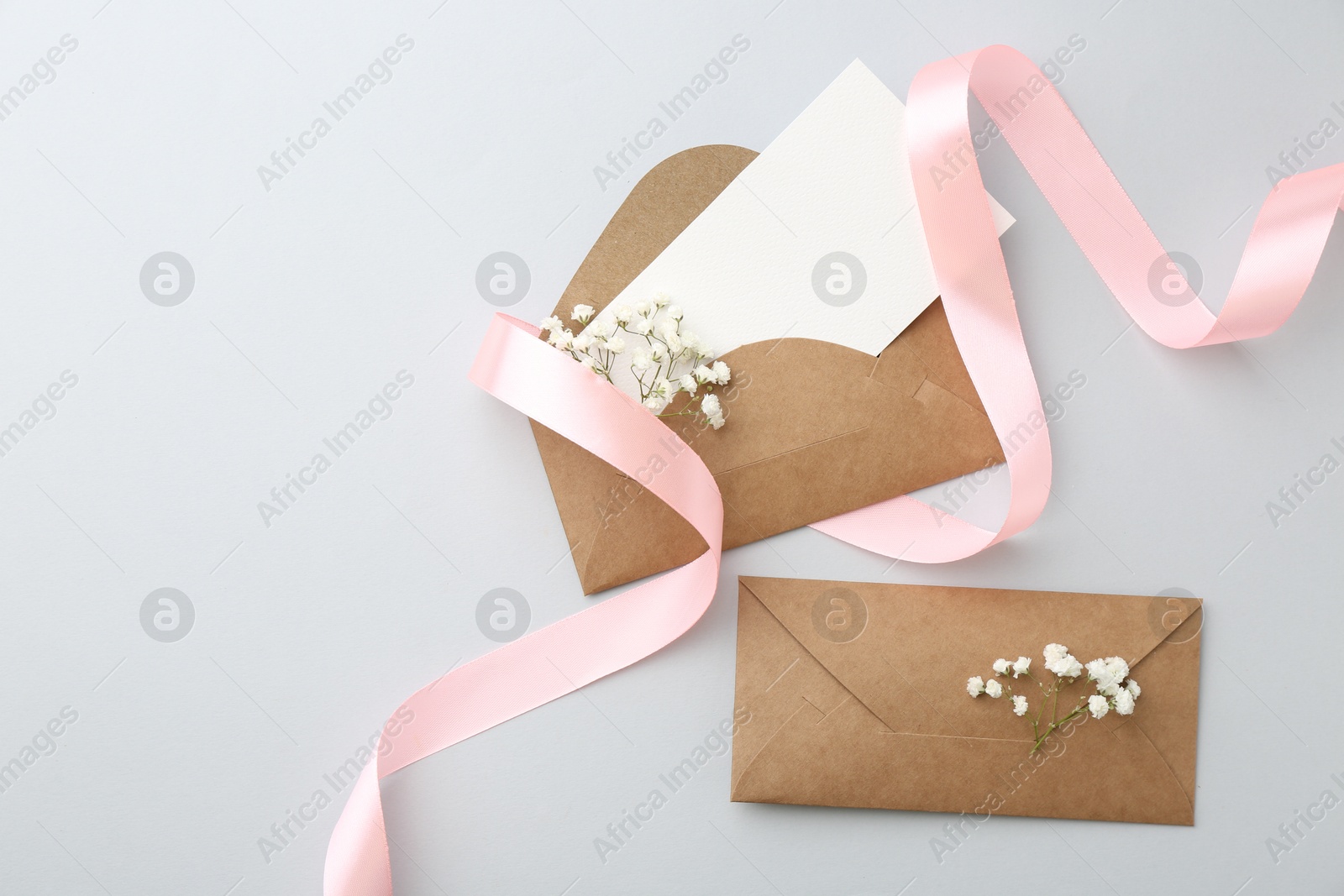 Photo of Blank card, envelopes, flowers and ribbon on light grey table, flat lay. Space for text