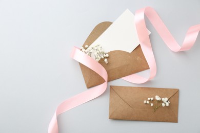 Photo of Blank card, envelopes, flowers and ribbon on light grey table, flat lay. Space for text