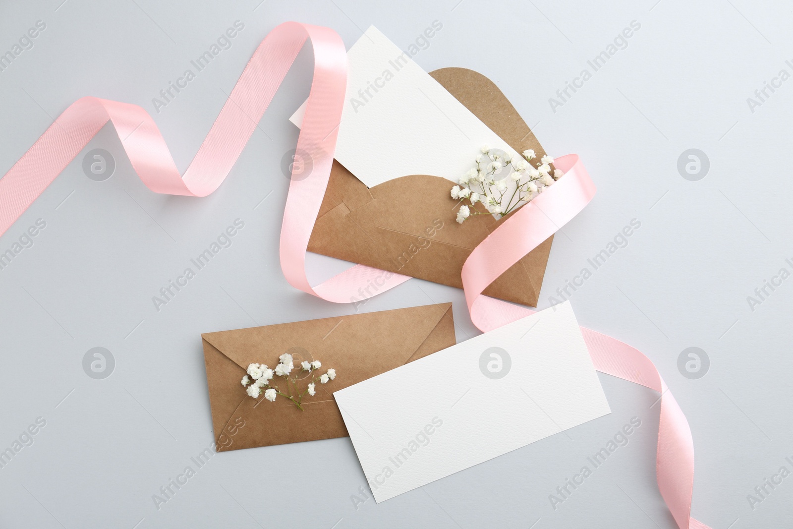 Photo of Blank cards, envelopes, flowers and ribbon on light grey table, flat lay