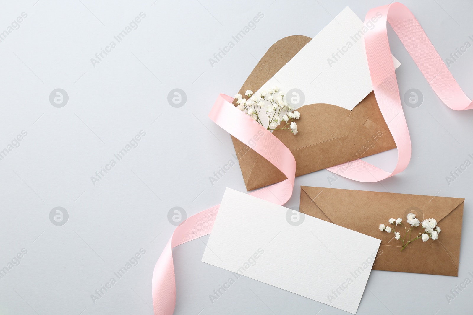 Photo of Blank cards, envelopes, flowers and ribbon on light grey table, flat lay. Space for text