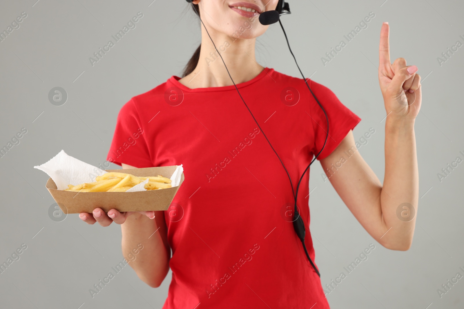 Photo of Fast-food worker holding paper container with fries on gray background, closeup