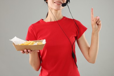 Photo of Fast-food worker holding paper container with fries on gray background, closeup