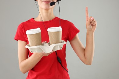 Fast-food worker with paper cups on gray background, closeup