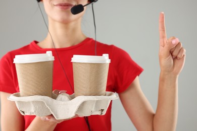 Fast-food worker with paper cups on gray background, closeup