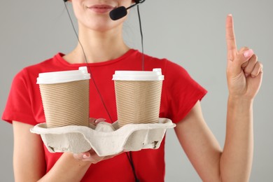 Fast-food worker with paper cups on gray background, closeup