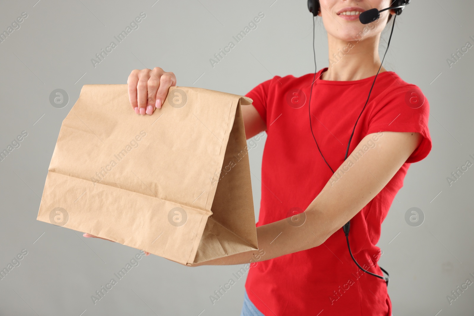 Photo of Fast-food worker with paper bag on gray background, closeup