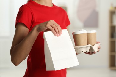 Photo of Fast-food worker with paper bag and cups indoors, closeup