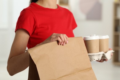 Photo of Fast-food worker with paper bag and cups indoors, closeup