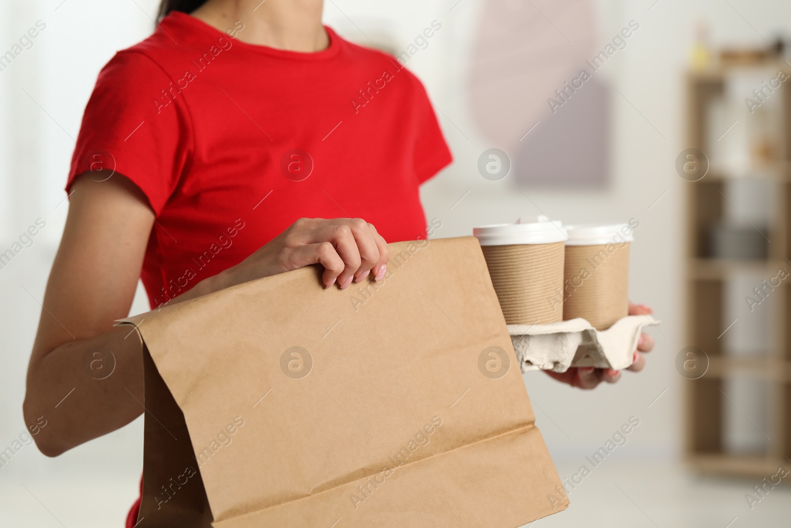 Photo of Fast-food worker with paper bag and cups indoors, closeup