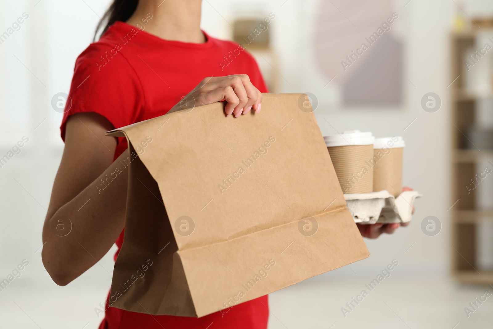 Photo of Fast-food worker with paper bag and cups indoors, closeup