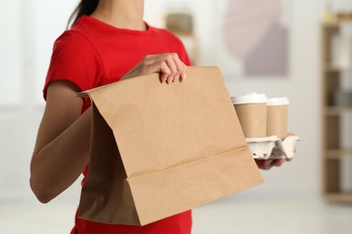 Photo of Fast-food worker with paper bag and cups indoors, closeup