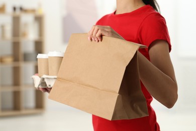 Photo of Fast-food worker with paper bag and cups indoors, closeup