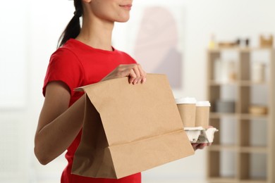 Photo of Fast-food worker with paper bag and cups indoors, closeup