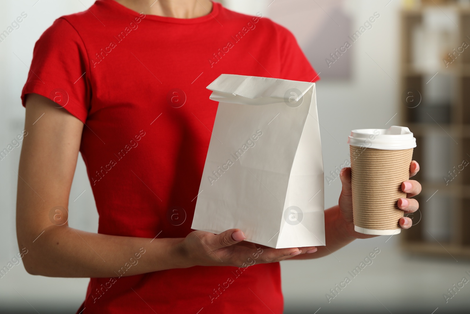 Photo of Fast-food worker with paper bag and cup indoors, closeup