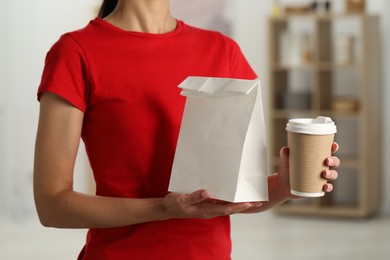 Photo of Fast-food worker with paper bag and cup indoors, closeup