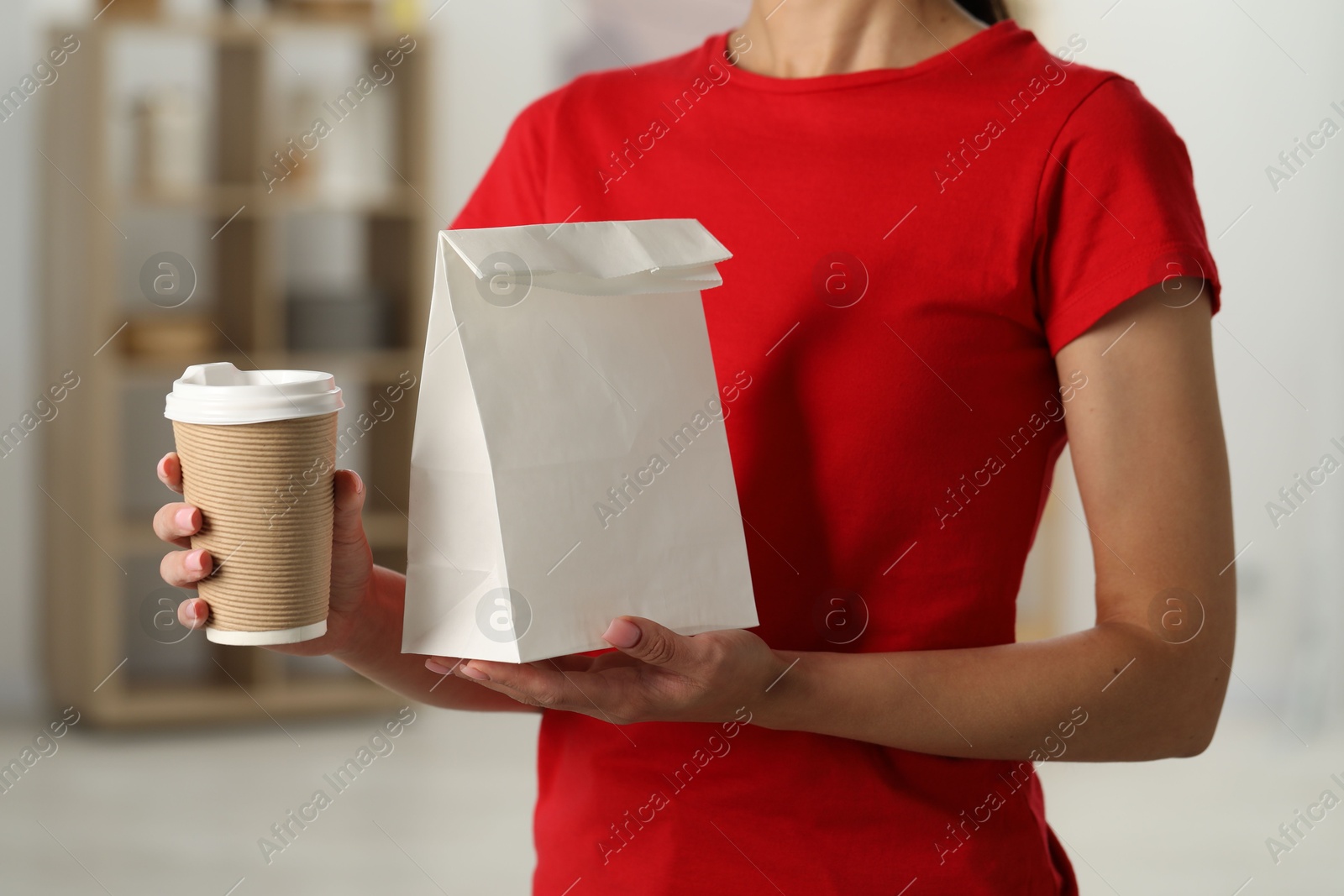 Photo of Fast-food worker with paper bag and cup indoors, closeup