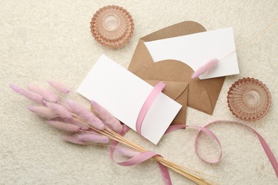 Photo of Blank cards, envelopes, flowers and ribbon on beige table, flat lay