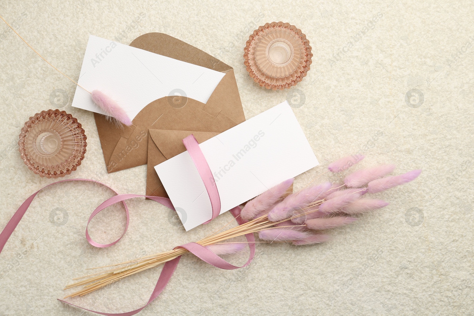 Photo of Blank cards, envelopes, flowers and ribbon on beige table, flat lay