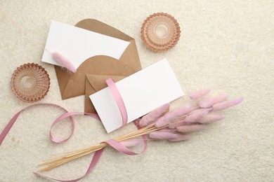 Blank cards, envelopes, flowers and ribbon on beige table, flat lay