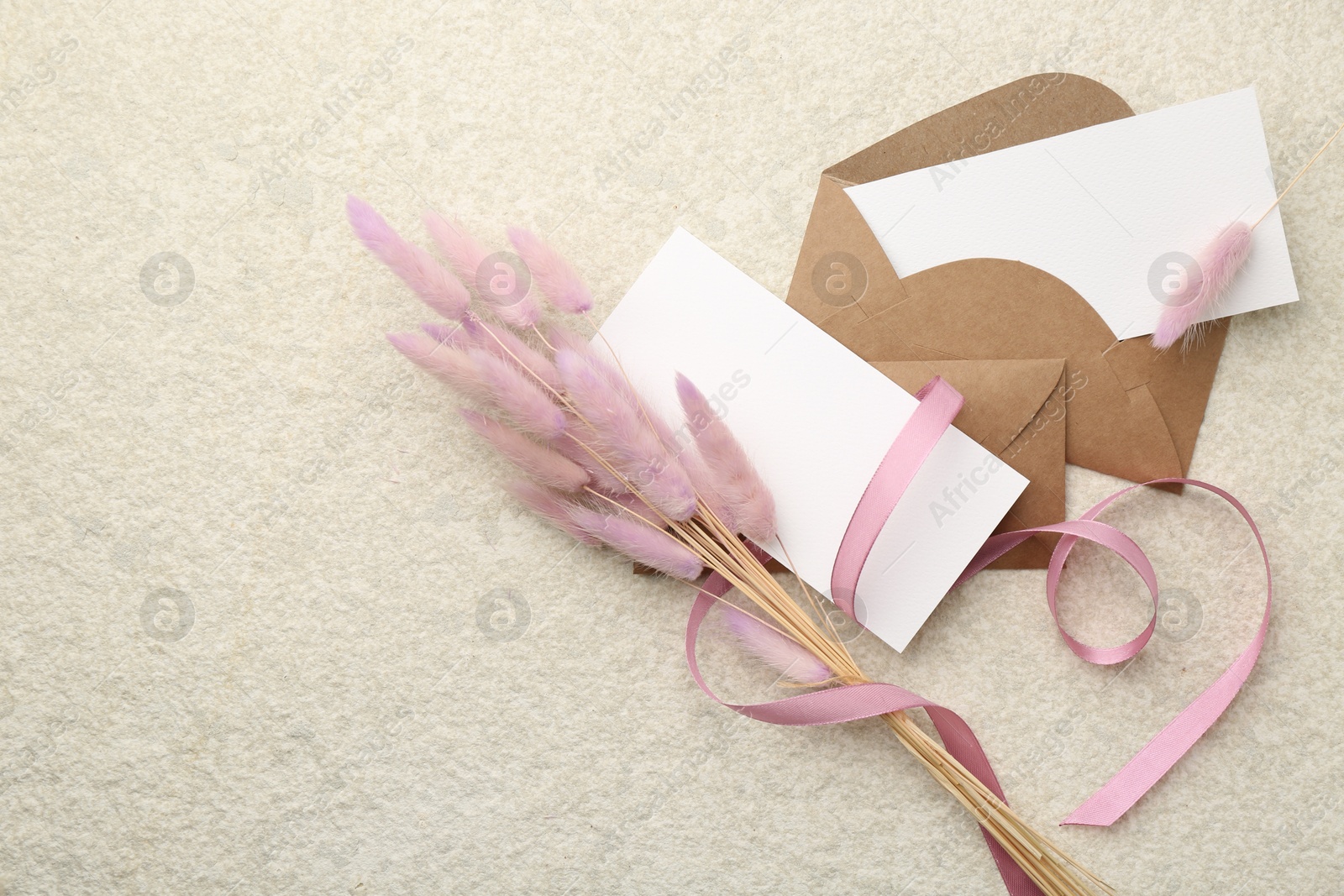 Photo of Blank cards, envelopes, flowers and ribbon on beige table, flat lay. Space for text