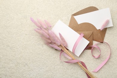 Blank cards, envelopes, flowers and ribbon on beige table, flat lay. Space for text