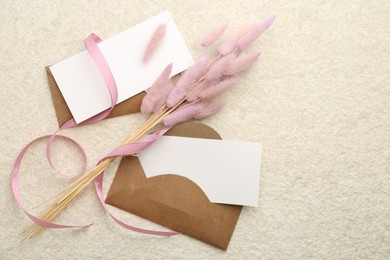 Blank cards, envelopes, flowers and ribbon on beige table, flat lay. Space for text