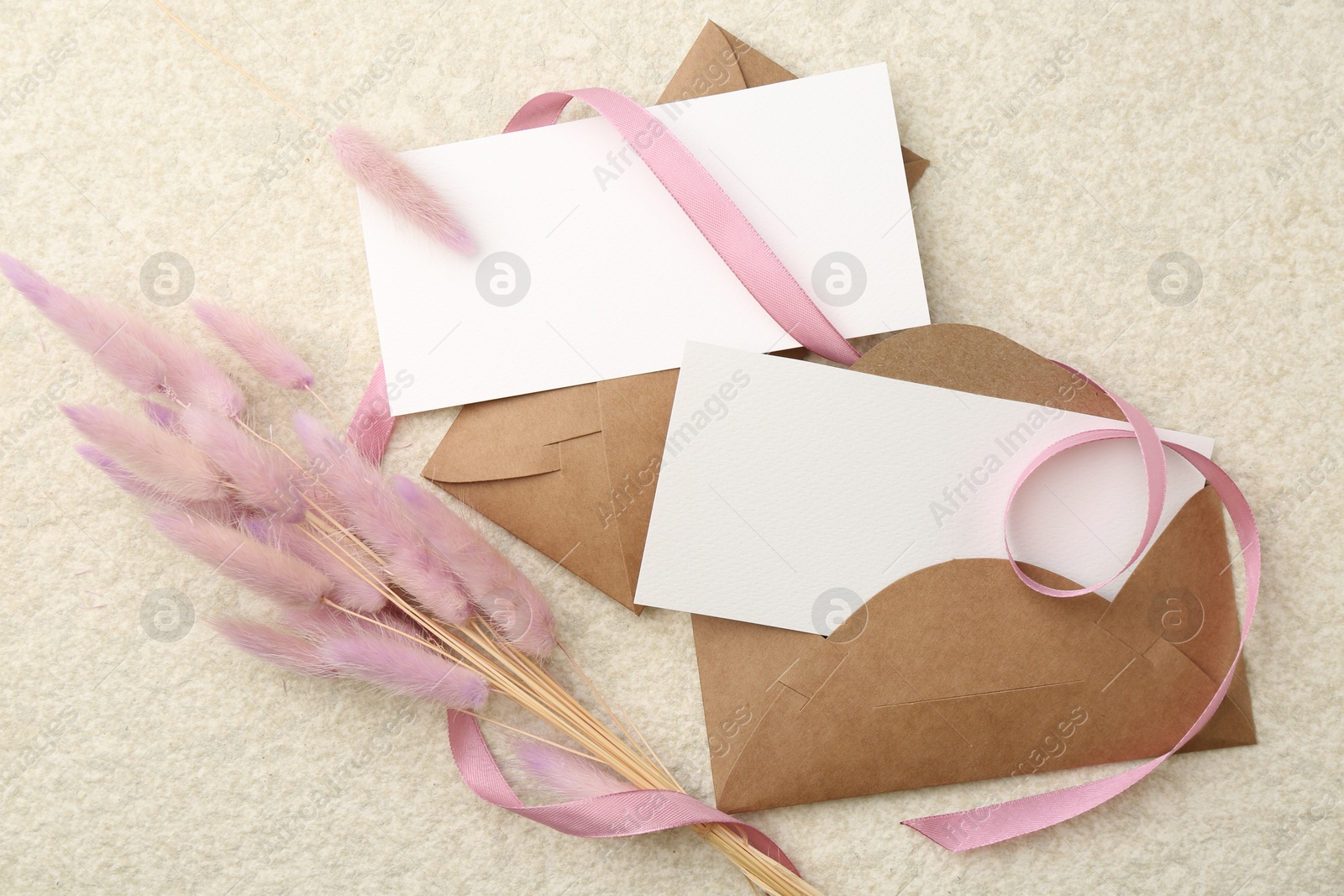 Photo of Blank cards, envelopes, flowers and ribbon on beige table, flat lay