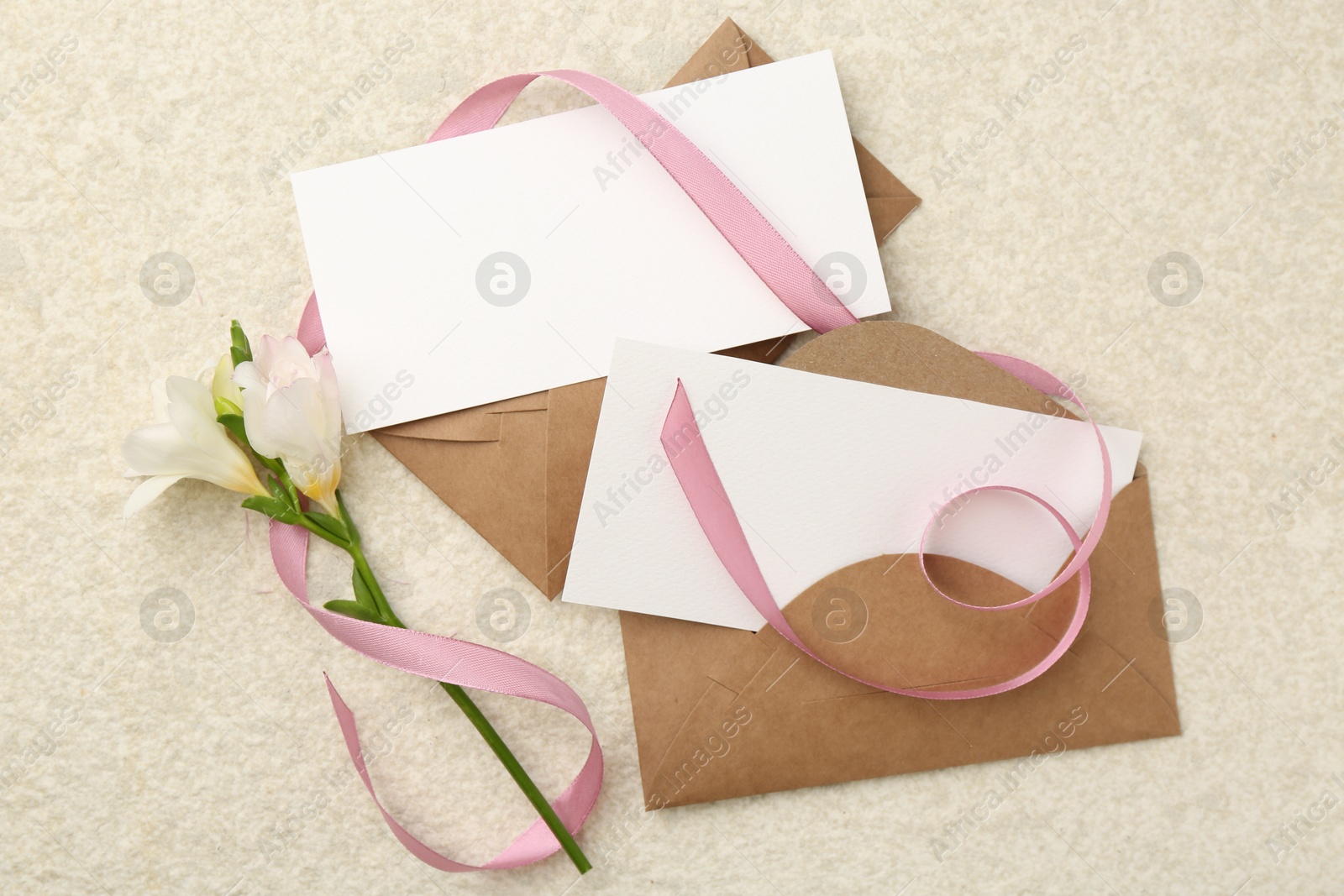 Photo of Blank cards, envelopes, flower and ribbon on beige table, flat lay