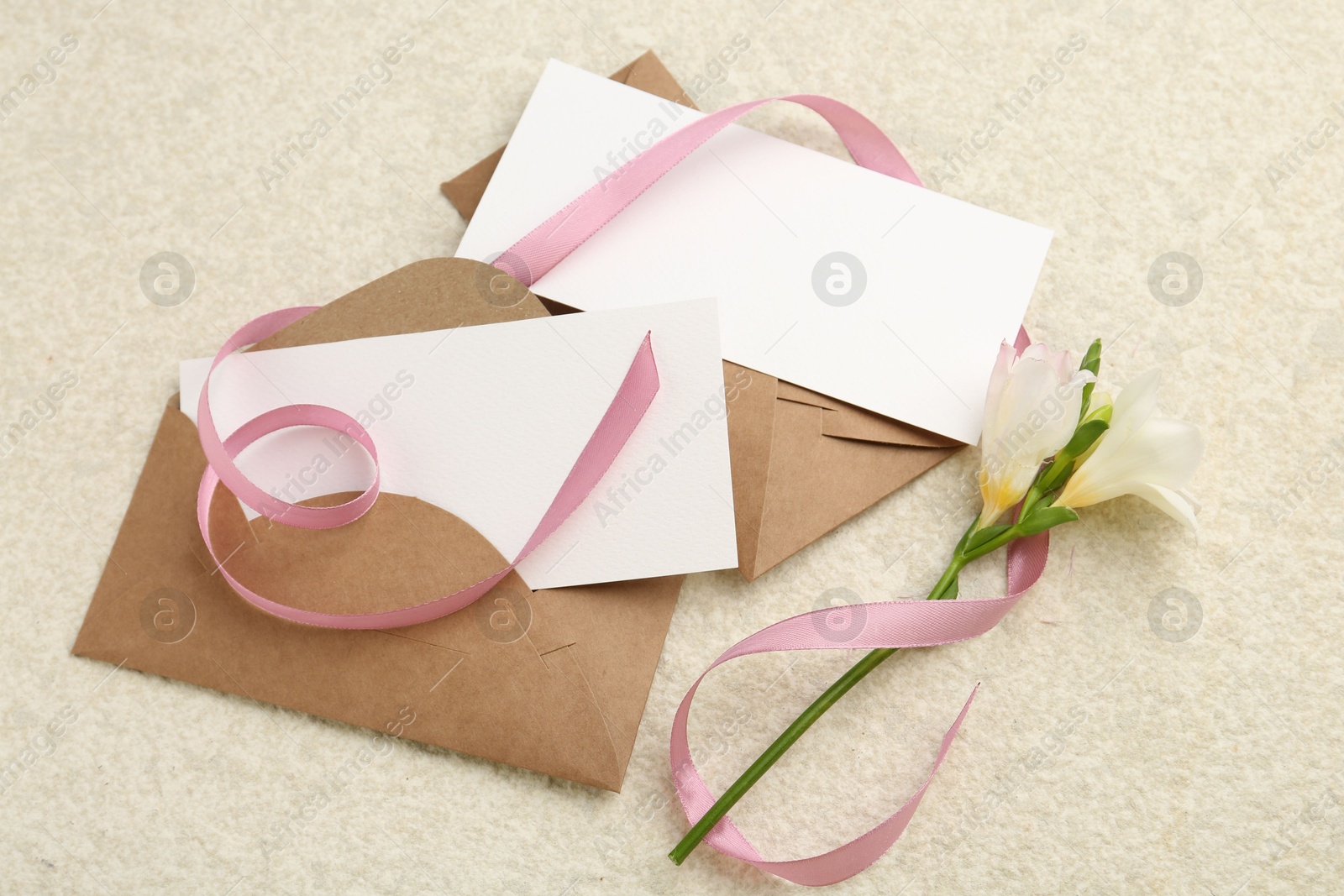 Photo of Blank cards, envelopes, flower and ribbon on beige table, flat lay