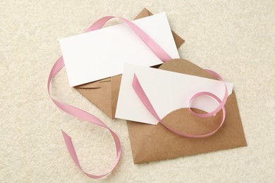 Photo of Blank cards, envelopes and ribbon on beige table, flat lay