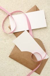 Photo of Blank cards, envelopes and ribbon on beige table, flat lay