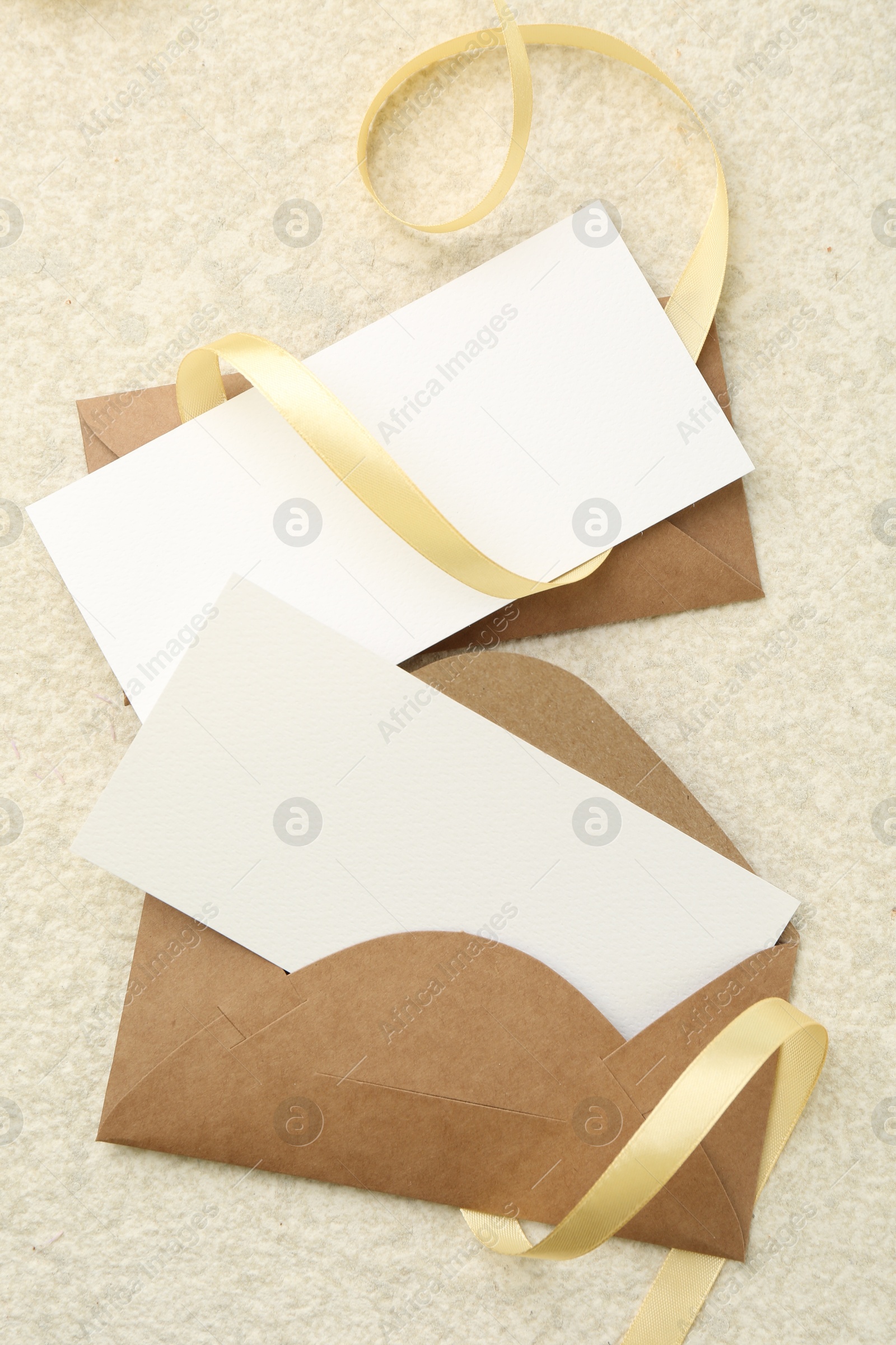 Photo of Blank cards, envelopes and ribbon on beige table, flat lay