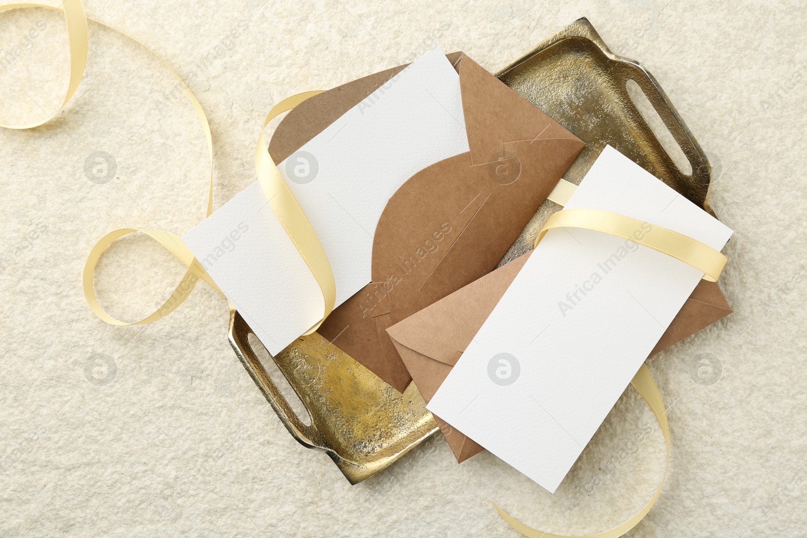 Photo of Blank cards, envelopes and ribbon on beige table, flat lay