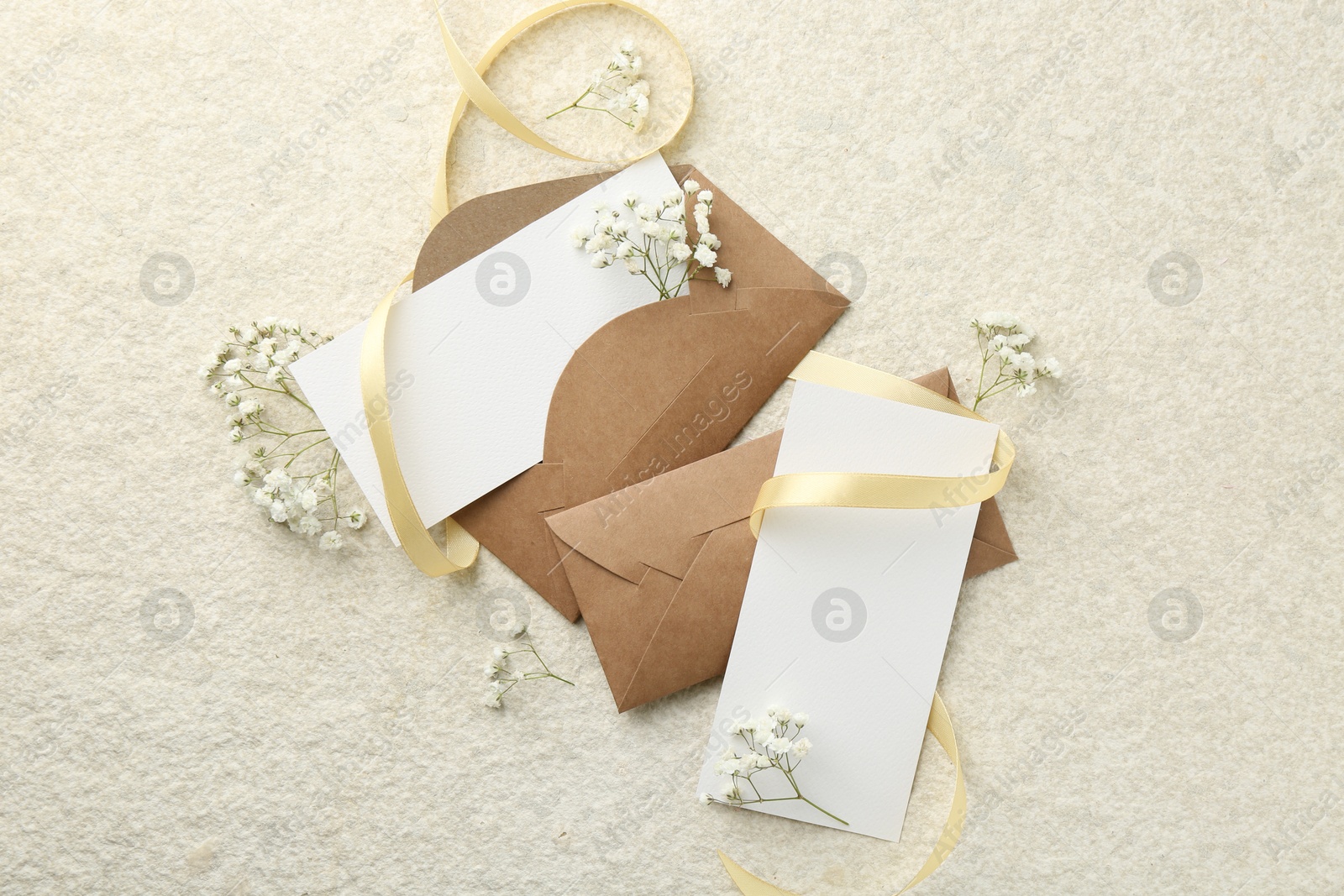 Photo of Blank cards, envelopes, flowers and ribbon on beige table, flat lay