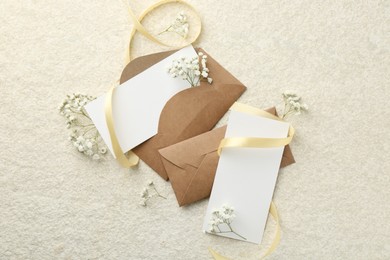 Blank cards, envelopes, flowers and ribbon on beige table, flat lay