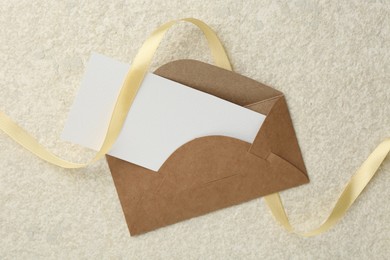 Photo of Blank card, envelope and ribbon on beige table, top view