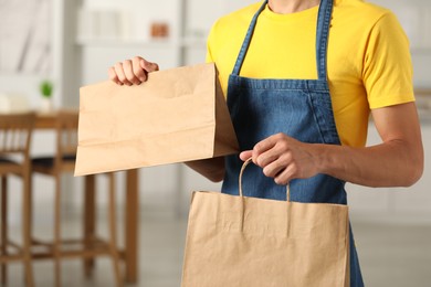 Photo of Fast-food worker with paper bags indoors, closeup