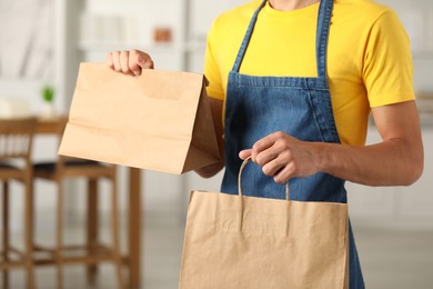 Photo of Fast-food worker with paper bags indoors, closeup