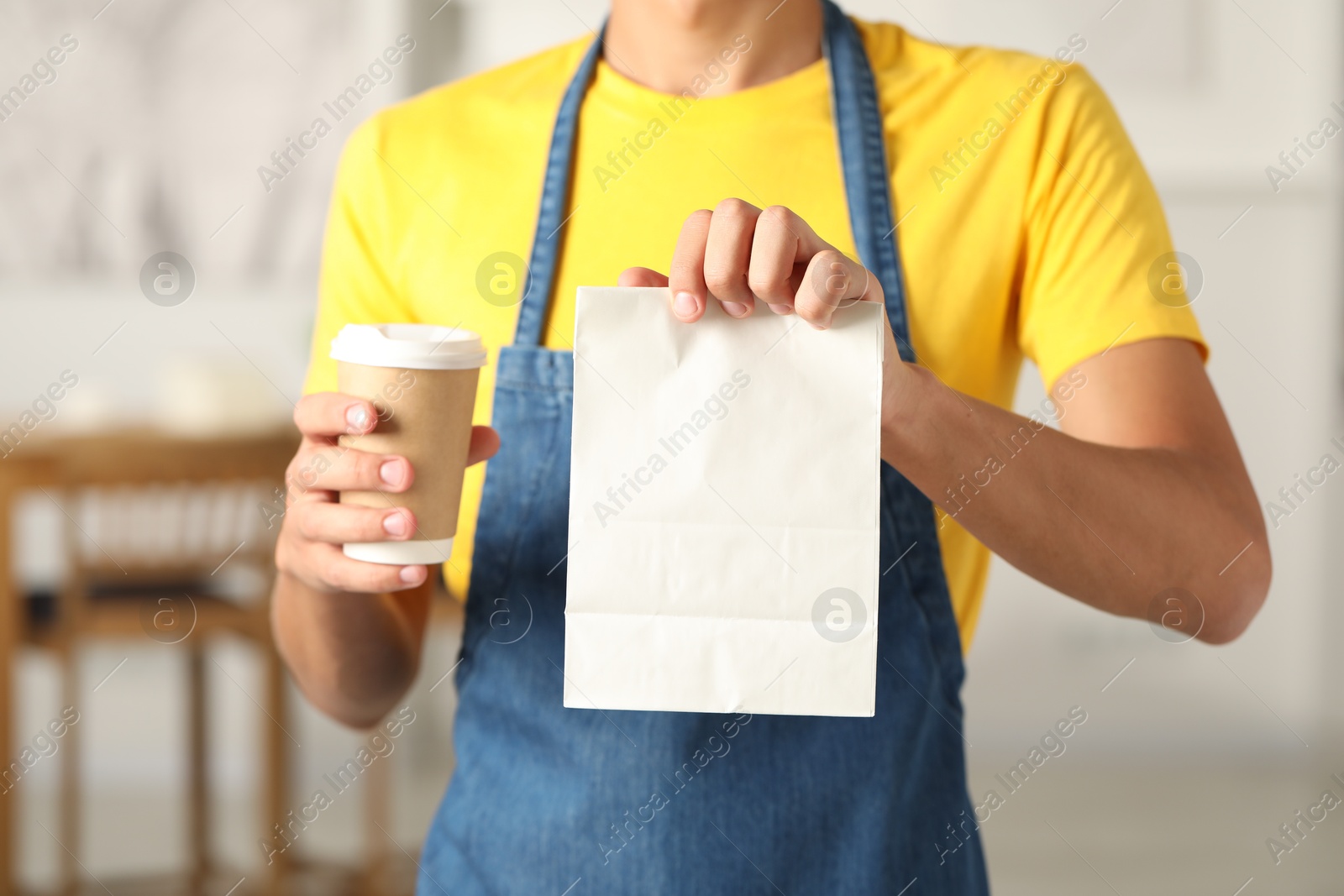 Photo of Fast-food worker with paper bag and cup indoors, closeup