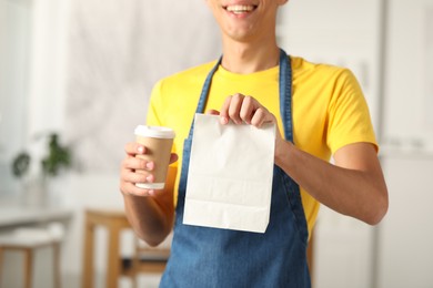 Fast-food worker with paper bag and cup indoors, closeup