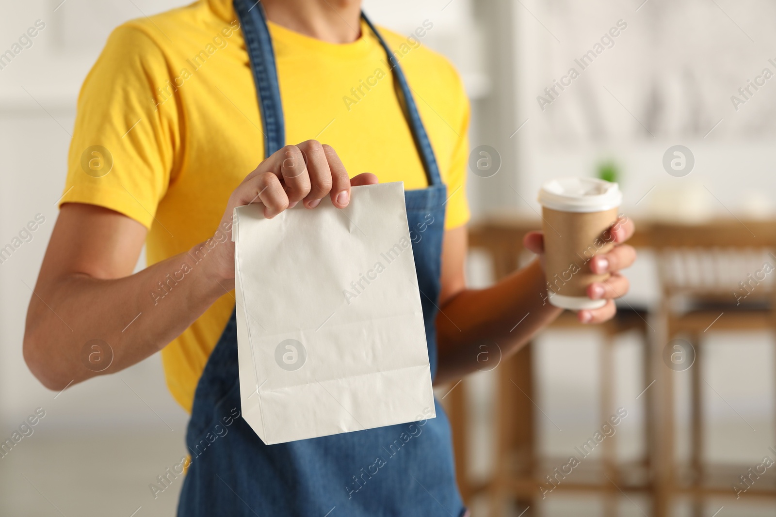 Photo of Fast-food worker with paper bag and cup indoors, closeup