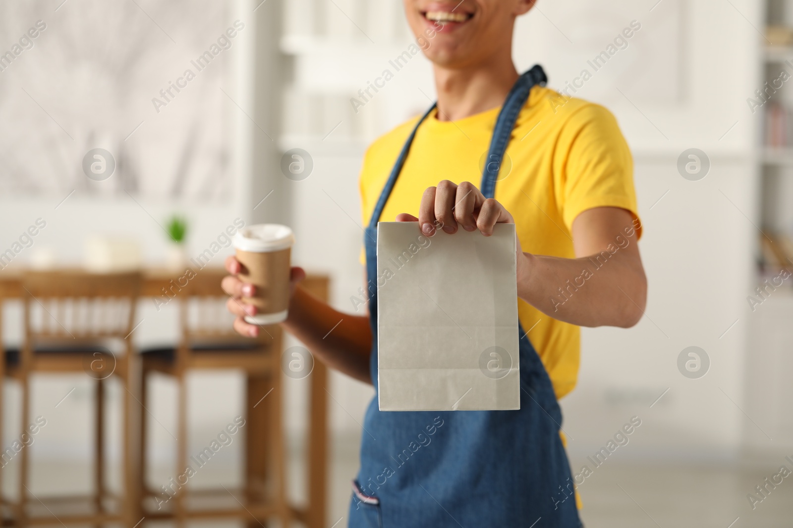 Photo of Fast-food worker with paper bag and cup indoors, closeup