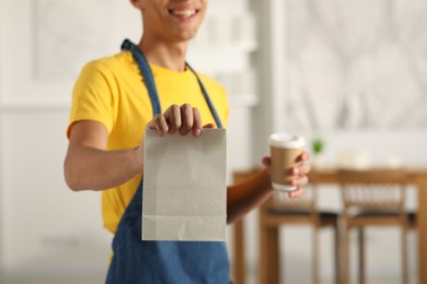 Fast-food worker with paper bag and cup indoors, closeup