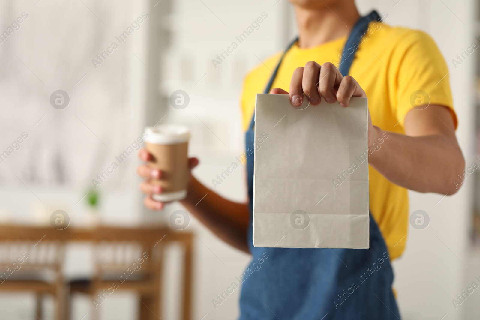 Photo of Fast-food worker with paper bag and cup indoors, closeup