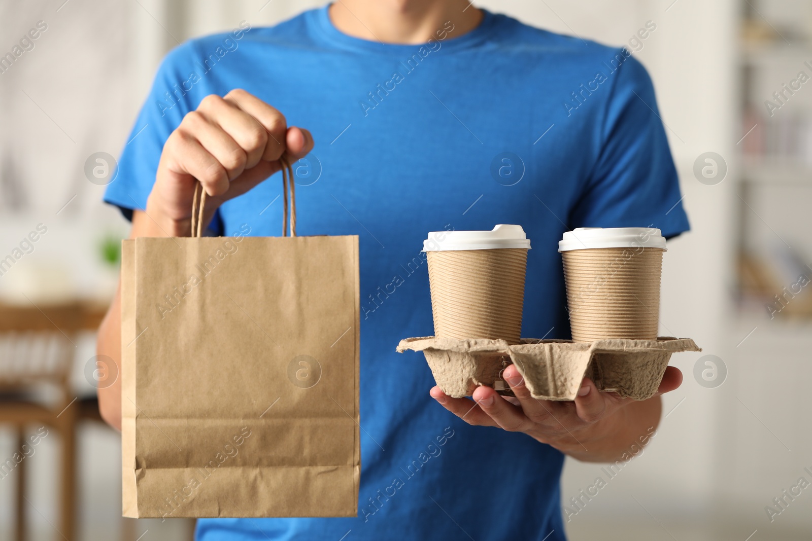 Photo of Fast-food worker with paper bag and cups indoors, closeup