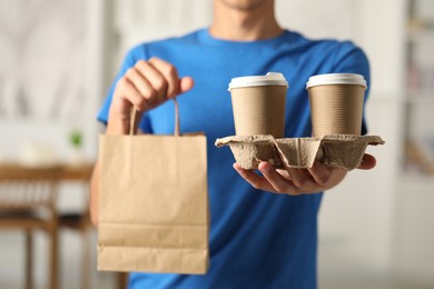 Photo of Fast-food worker with paper bag and cups indoors, closeup